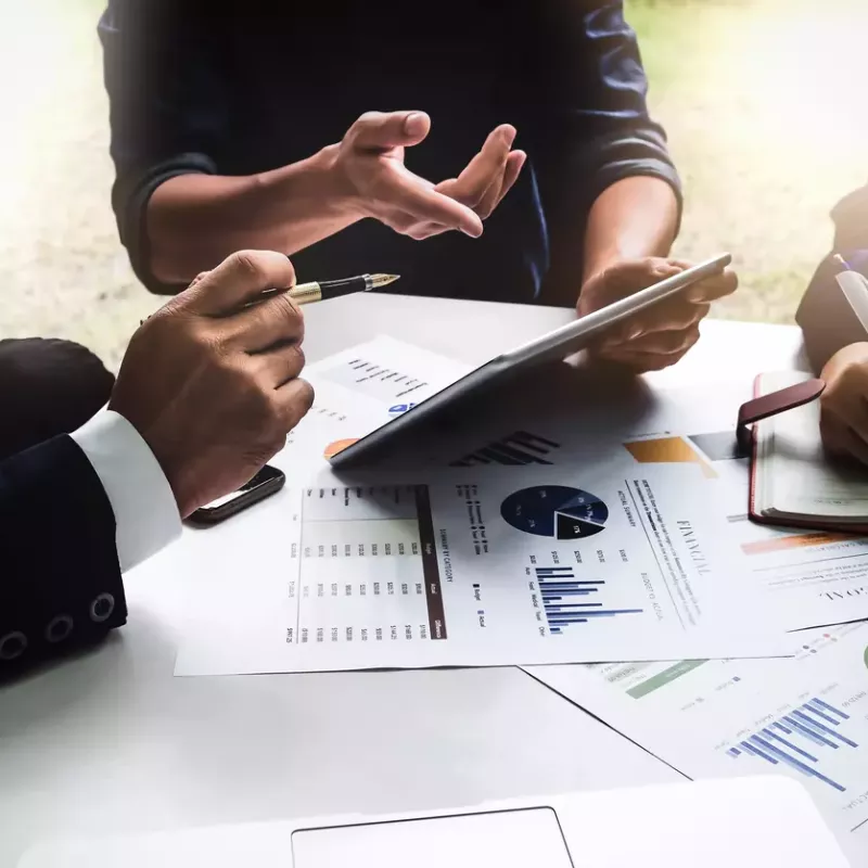 Close up of the torso, arms and hands of business professionals around a conference table reviewing charts and tables.
