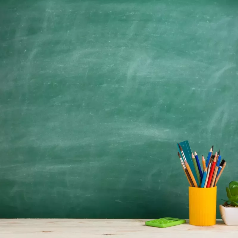 Blank green chalkboard with yellow cup of drawing utensils to the right.