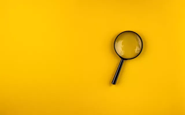 Magnifying glass lies on a yellow background with shadows in the left bottom and top right corners.