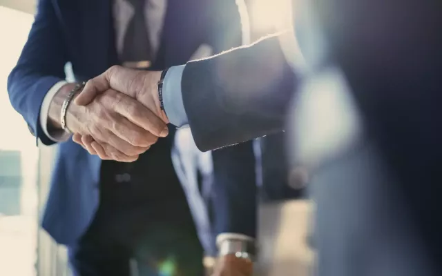 Two businessmen in suits shaking hands in a close of photo not showing their faces with lens flare.