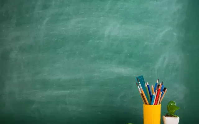 Blank green chalkboard with yellow cup of drawing utensils to the right.