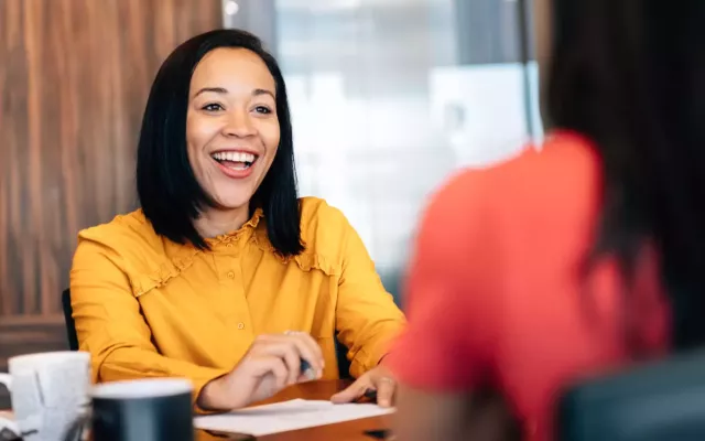 Sales rep laughs while chatting at a desk with sales leadership.