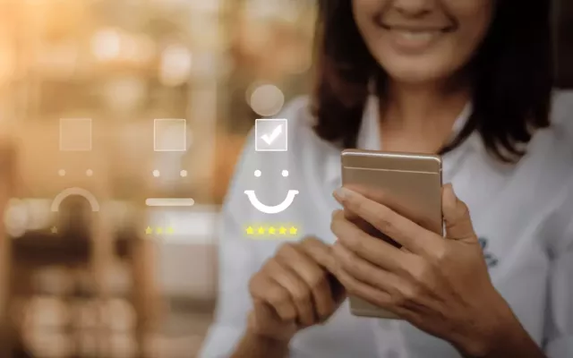 Young woman wearing glasses smiles are her smart phone. An overlay of frown, neutral and smile graphics show a highlight smile with a check mark.