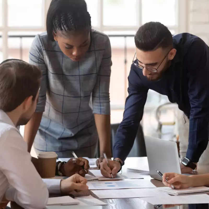 Young professionals wearing business casual clothing discuss sales plans at a conference table.