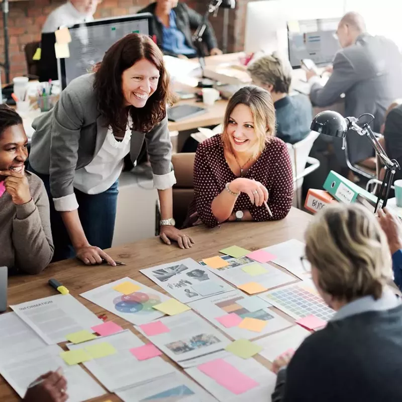 A group of happy coworkers meet around a conference table with papers and sticky notes; Rise and Shine: Salesforce Digital Magazine from Xactly