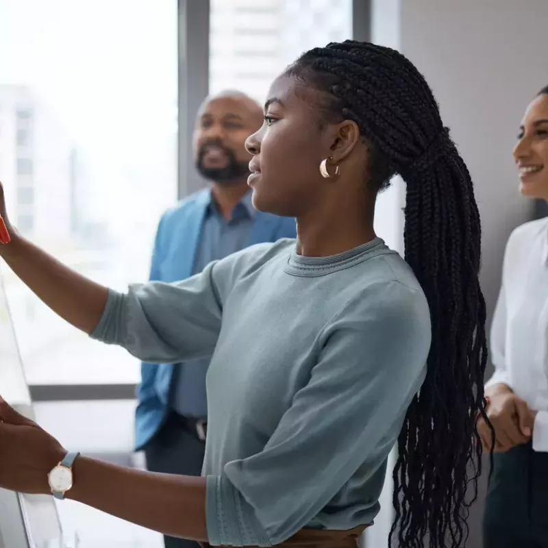 Diverse group of young professionals gathers to discuss buyer personas in a modern office with one woman working on a white board.