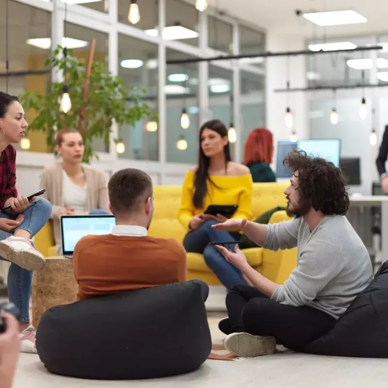 Sales and marketing colleagues at a start-up meet in an open space using quirky seating and laptops.