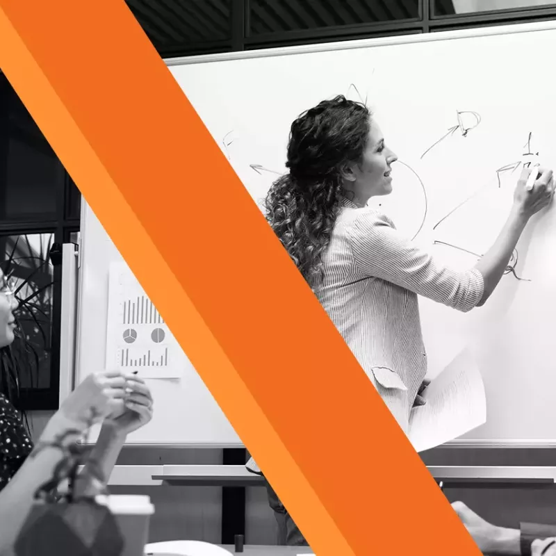 black and white woman writing on whiteboard as colleagues watch