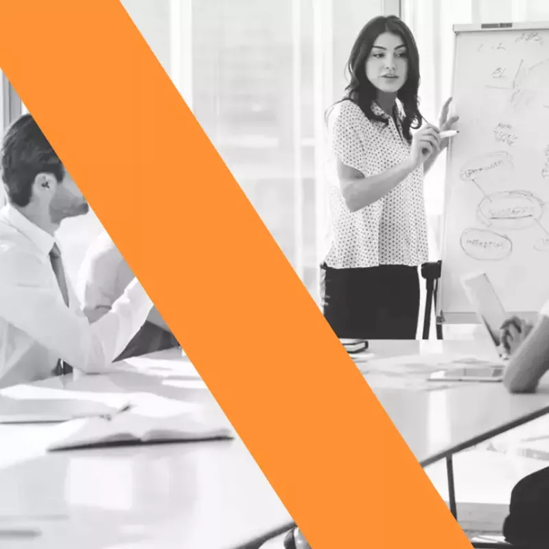 A black and white photo of a woman standing at chart turned and facing a group of people sitting at a conference table blog header for Xactly.