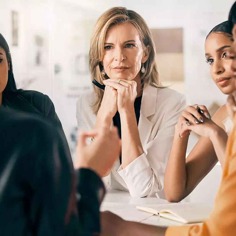 A group of professionals sit closely around a conference table talking intently about the MetaCompliance case study with their elbows on the table.