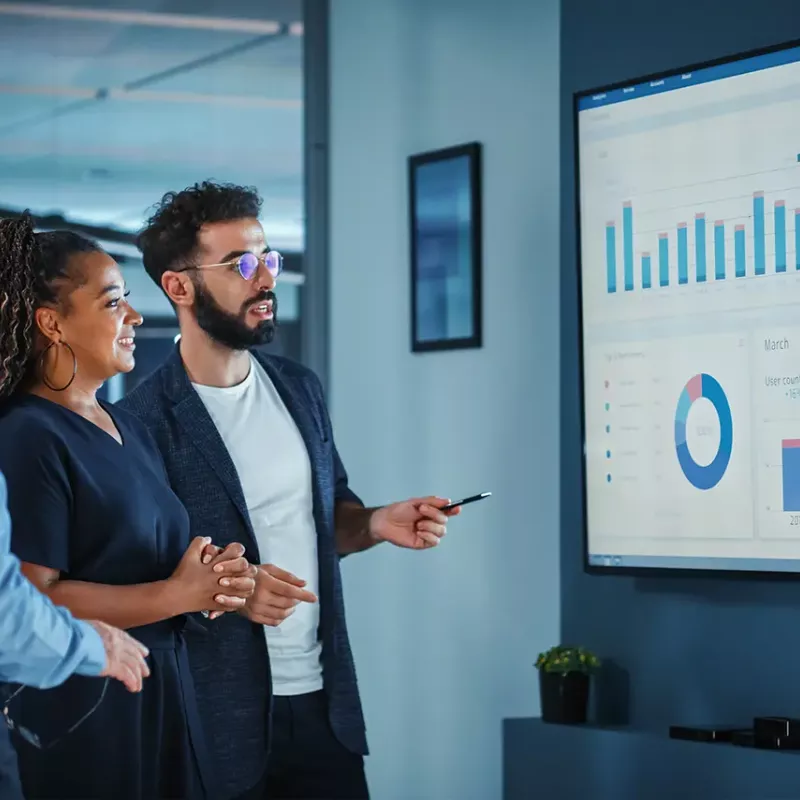 man standing next to woman and man all looking at large screen with graphics