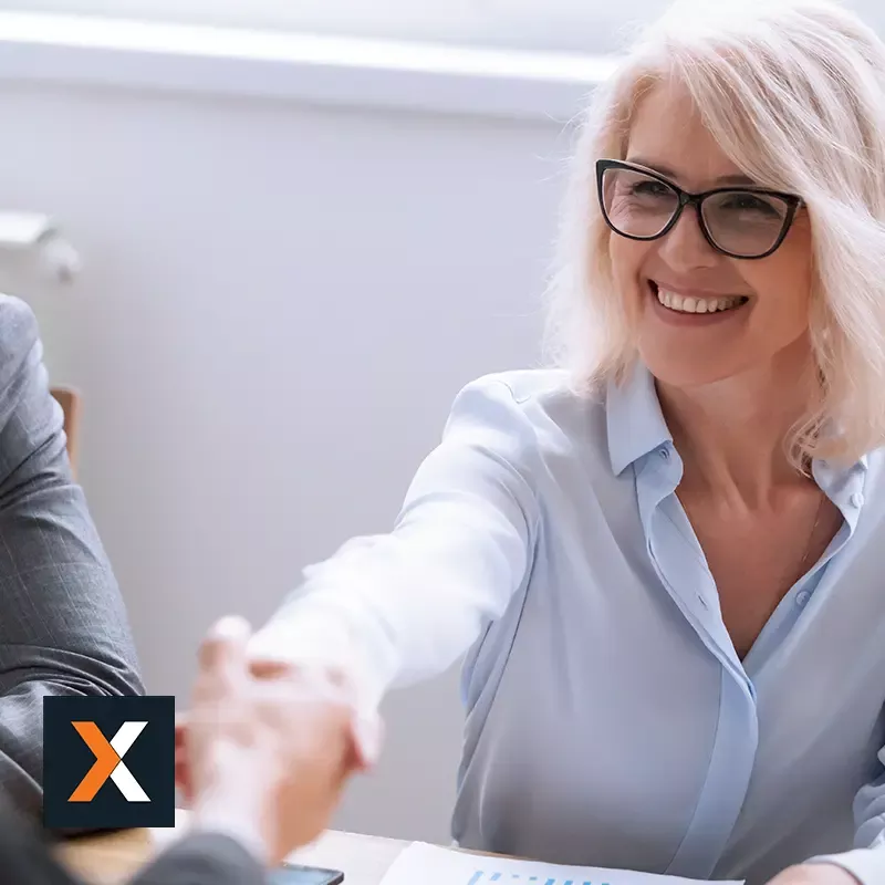 business woman wearing glasses at computer handshaking with another business professional