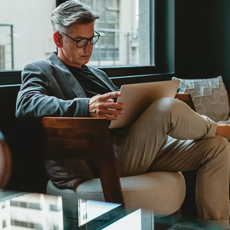 Man sitting in a chair with his legs crossed with a laptop in his lap.