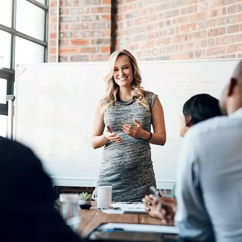 A woman confidently presenting to a group of attentive individuals during a professional meeting.