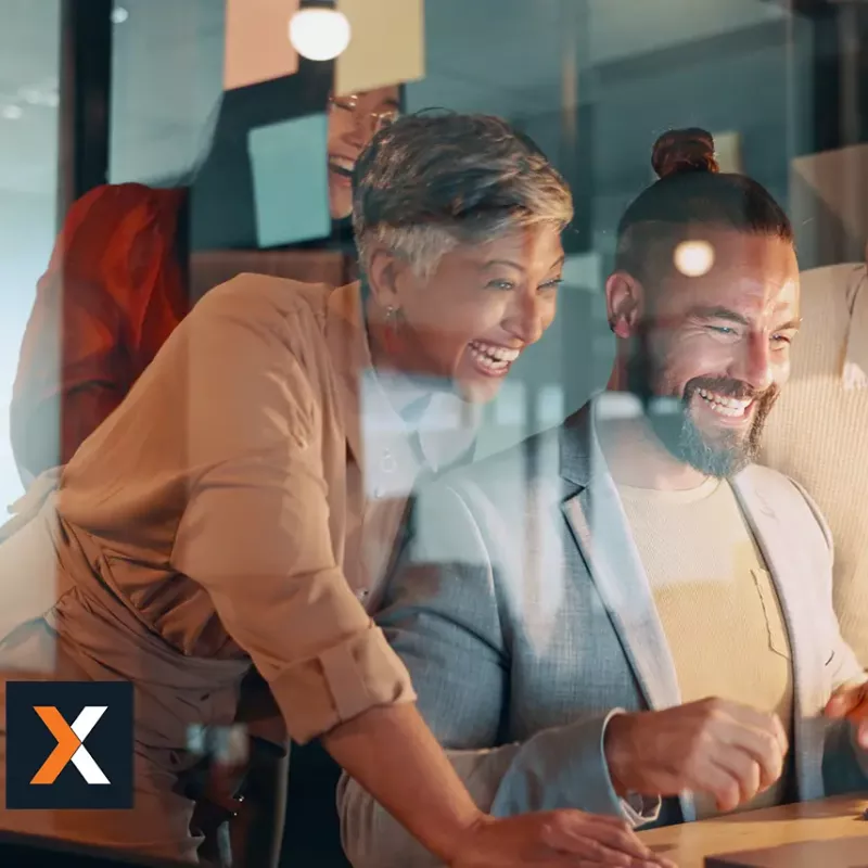 Group of coworkers sitting at table working and smiling off one laptop