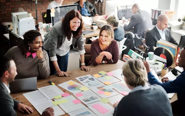 A group of happy coworkers meet around a conference table with papers and sticky notes; Rise and Shine: Salesforce Digital Magazine from Xactly