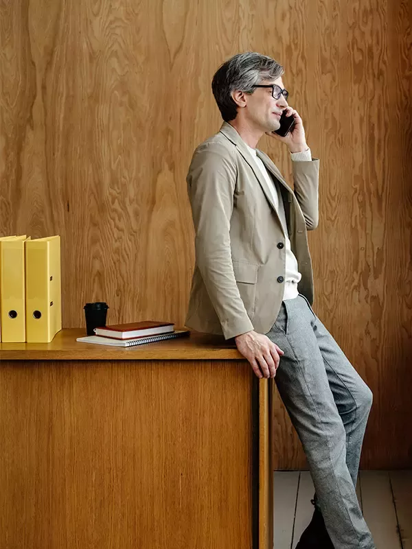 Engaged in a phone call, a man sits on a desk, handling business with ease.