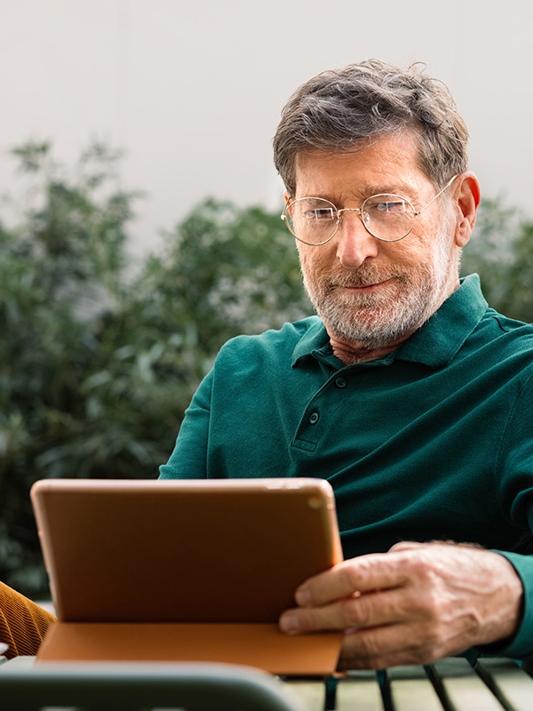 A tech-savvy man in a green shirt uses a tablet while relaxing on a bench.
