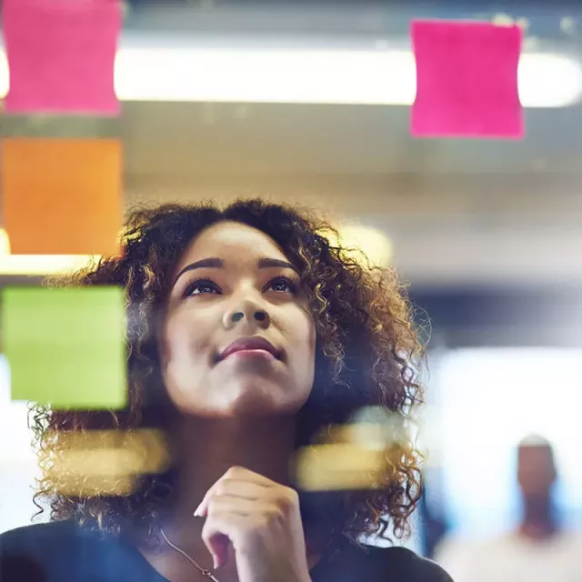 A focused woman studying a post-it note on a wall, deep in thought, seeking inspiration or a reminder of something important.