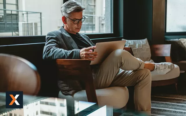 Man sitting in a chair with his legs crossed with a laptop in his lap.