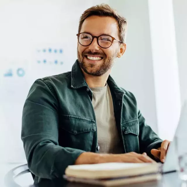 Happy man with glasses using laptop at a desk.