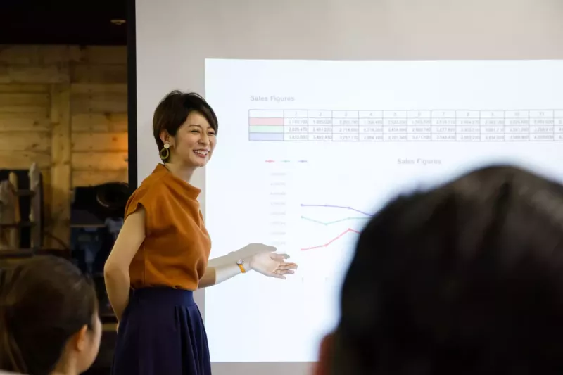 Smiling business woman presents projected sales figures in front of a screen.
