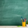 Blank green chalkboard with yellow cup of drawing utensils to the right.